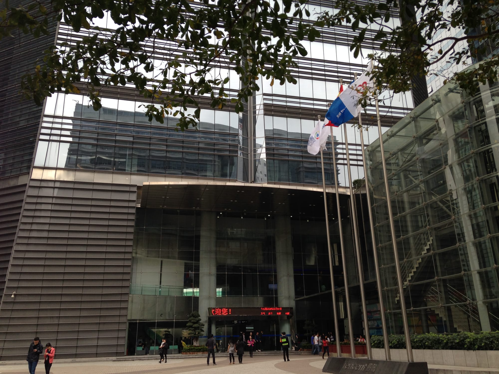 Entrance to the Tencent Building in Shenzhen, with flags outside its glass facade and pedestrians near the doors